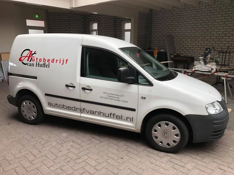 Witte bestelbus met rood-zwart logo, adres en website op de zijkant