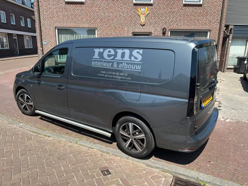 Grijze bestelauto van opzij met grijze belettering en contactgegevens op de zijruit