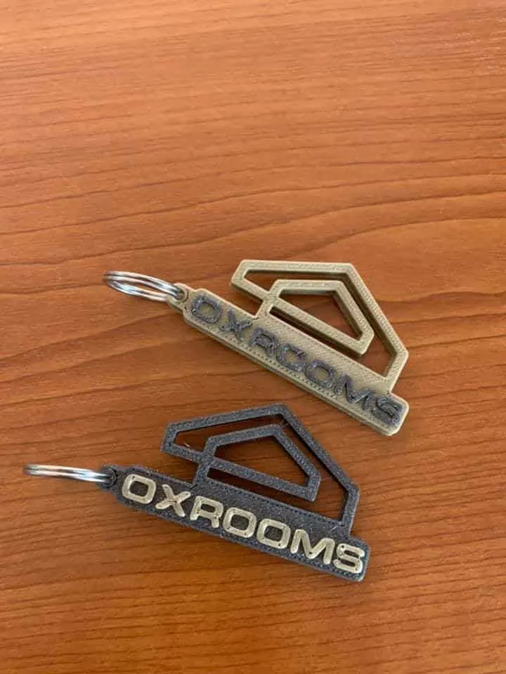 Twee 3D-geprinte sleutelhangers in goud en zwart met logo