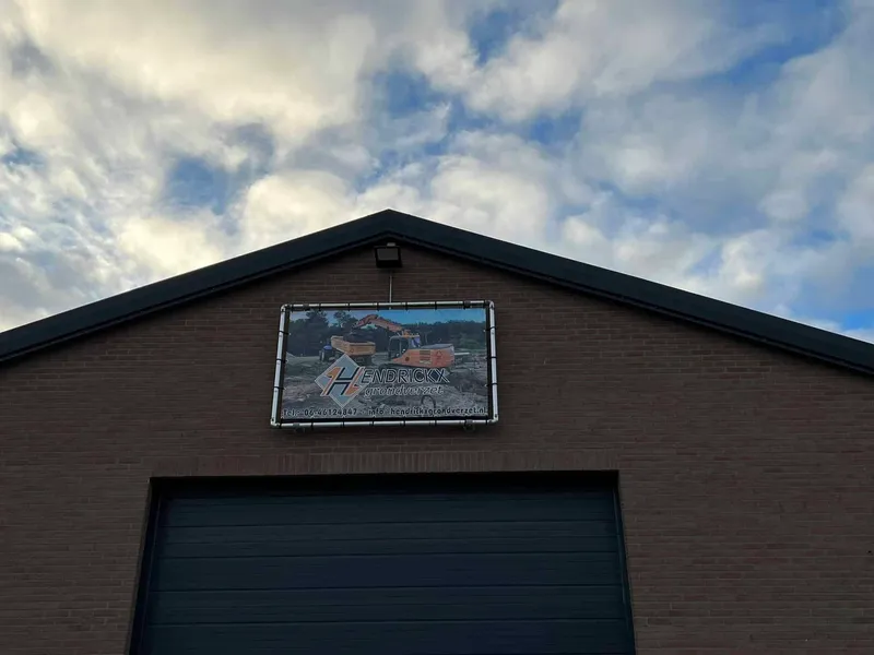 Bedrijfspand met spandoek in buisframe boven de roldeur tegen een wolkenlucht