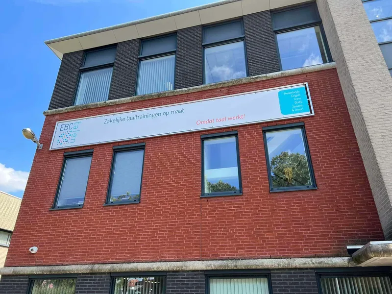 Lang wit spandoek met logo en slogan tussen de ramen van een kantoorgebouw