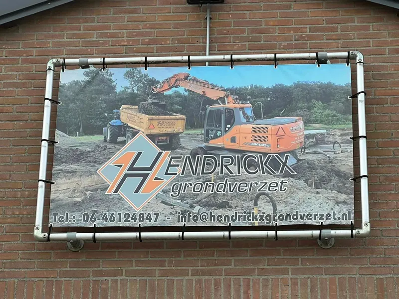 Close-up van spandoek in buisframe met foto van graafmachine en kiepwagen en logo
