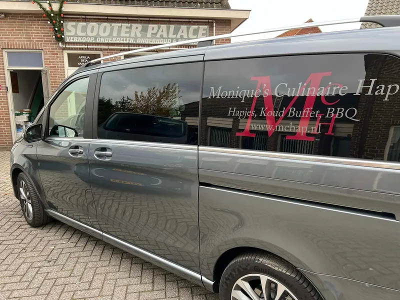 Grijze personenbus met witte en rode belettering en website op de zijruiten