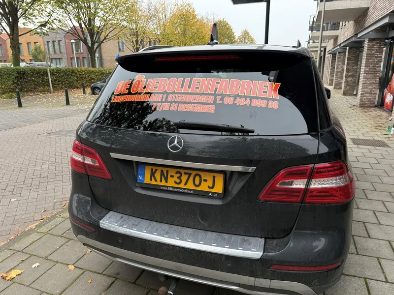 Donkere SUV van achteren met rood-gele belettering en contactgegevens op de achterruit