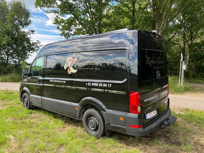Zwarte bedrijfswagen schuin van achteren met goudkleurig logo en diensten