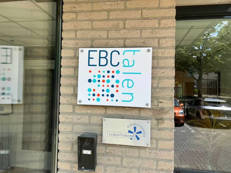 Wit naambord met logo van gekleurde stippen naast een entree met intercom