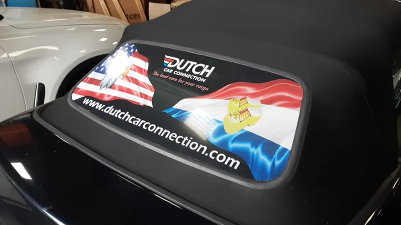 Achterruit van een cabriokap met bedrukking van vlaggen, logo en website