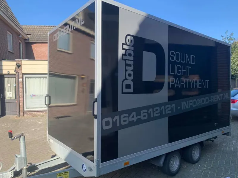 Aanhangwagen schuin van voren met groot logo en telefoonnummer op de zijkant