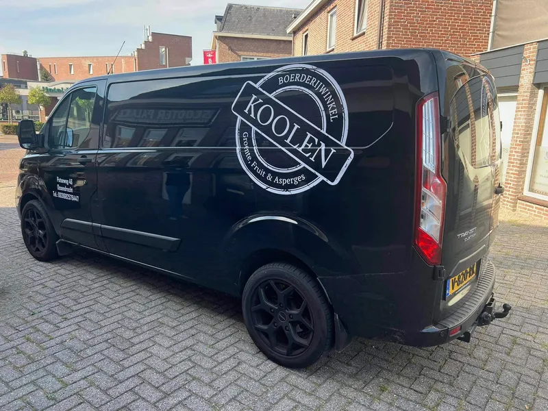 Zwarte bestelbus schuin van achteren met groot wit stempellogo en adres op het portier