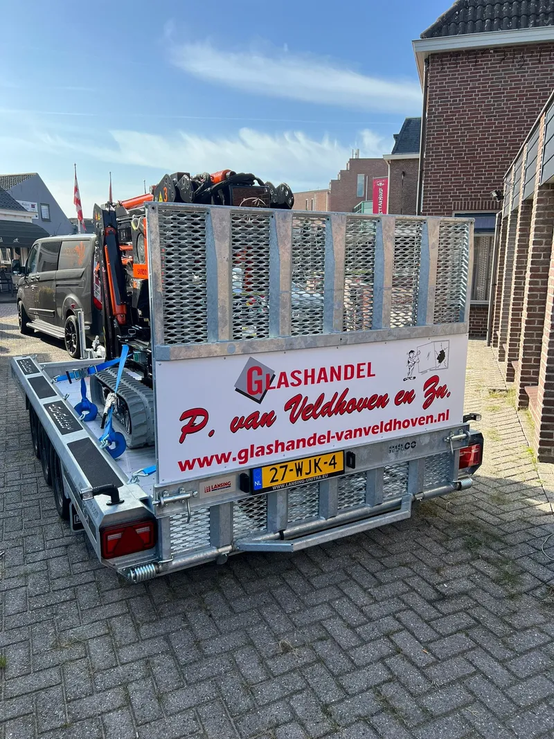 Machinetransporter met hoogwerker en wit achterbord met rode belettering en website
