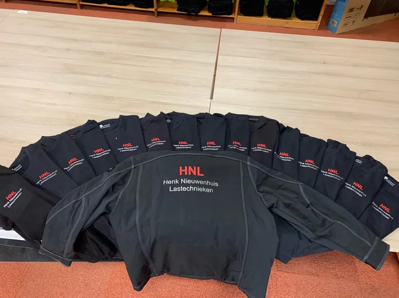 Waaier van zwarte shirts en een jas met rode afkorting en witte bedrijfsnaam