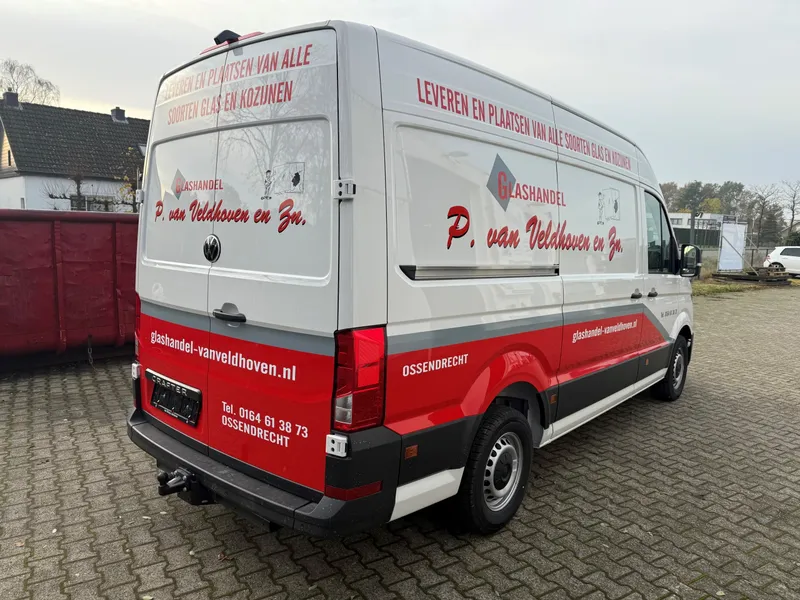Witte bestelbus schuin van achteren met rode band, logo en slogan op deuren en zijkant