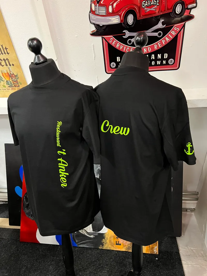 Twee zwarte shirts op paspoppen met neongele opdruk en anker op de mouw