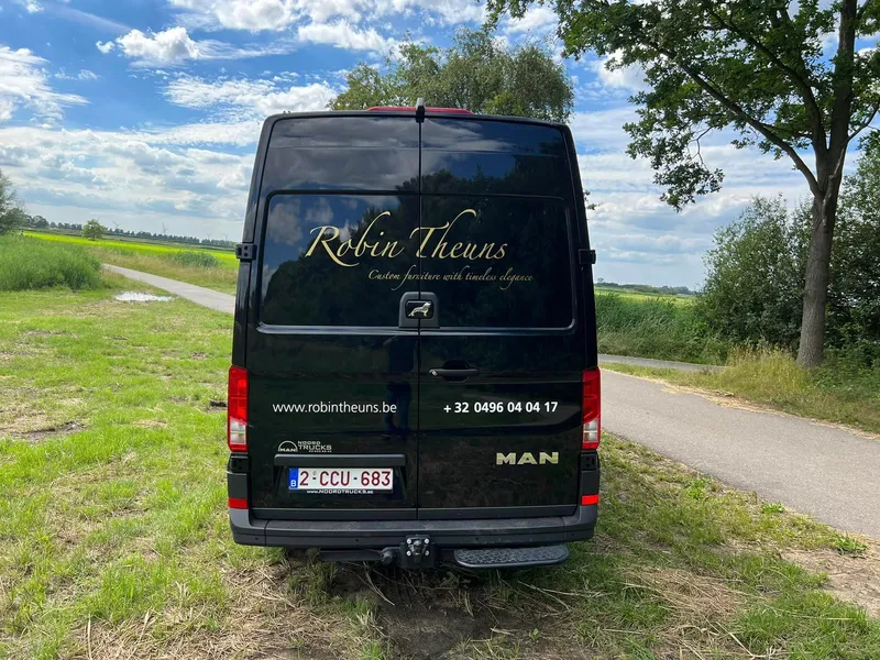 Zwarte bedrijfswagen van achteren met goudkleurige tekst op de achterruit