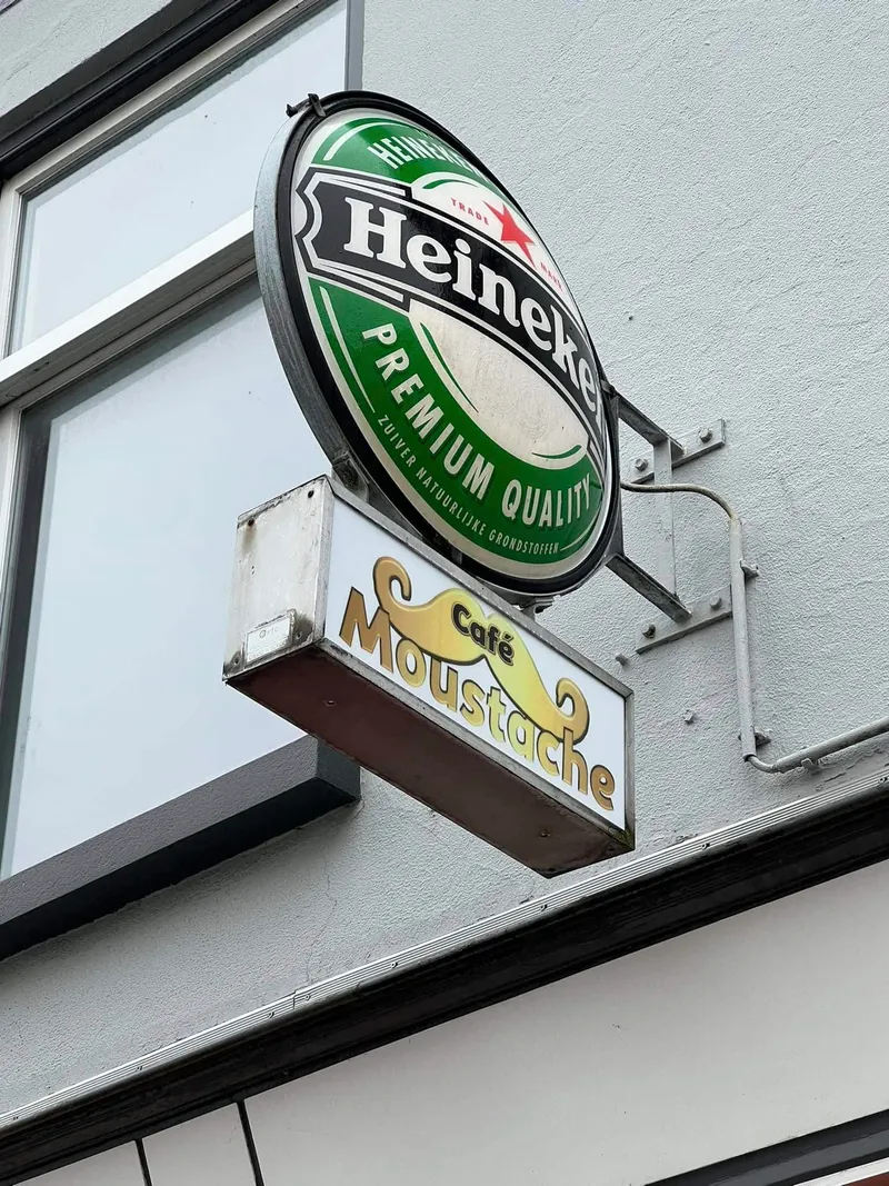 Uithangende lichtbak met snorlogo onder een ronde lichtreclame van een biermerk