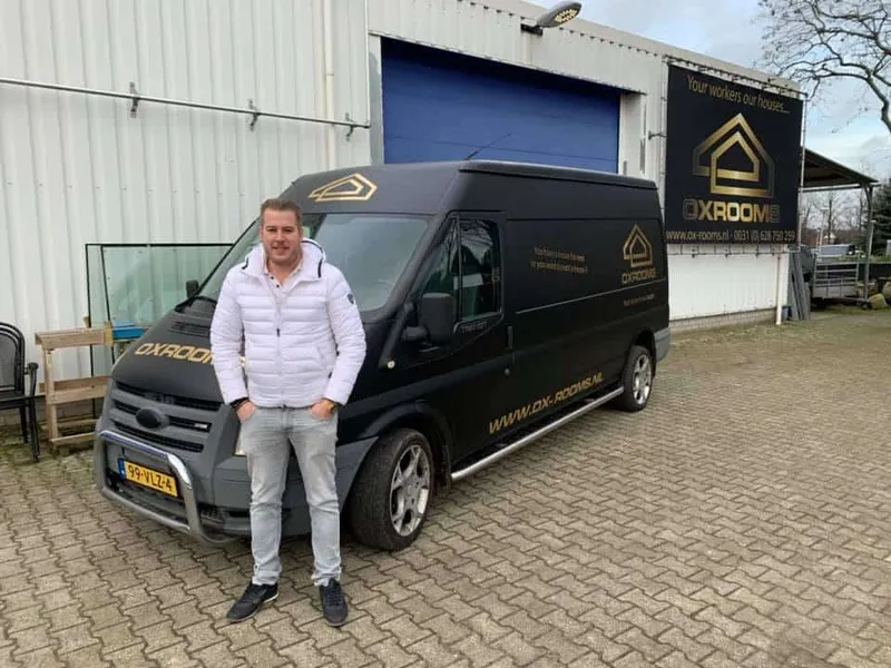 Zwarte bestelbus met gouden belettering voor een bedrijfspand met reclamebord