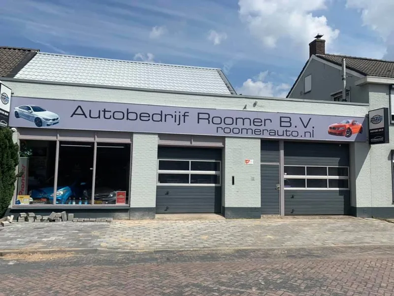 Brede gevelreclame met bedrijfsnaam, website en auto-afbeeldingen boven de etalage
