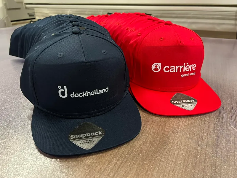 Rij donkerblauwe en rode snapback caps met wit bedrukt logo