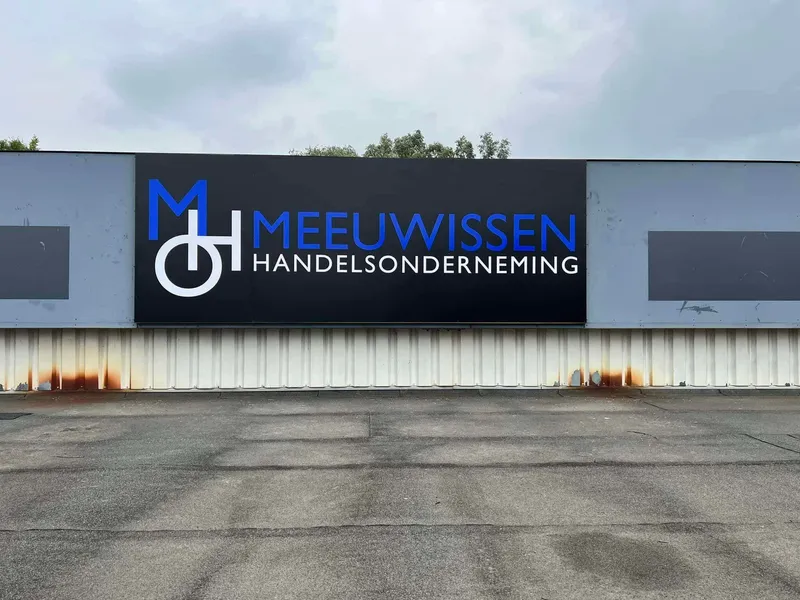 Zwart gevelpaneel met blauw-wit logo en bedrijfsnaam op een bedrijfspand