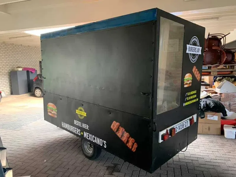 Zwarte verkoopwagen schuin van achteren met logo, snackfoto's en tekst op zij- en achterkant