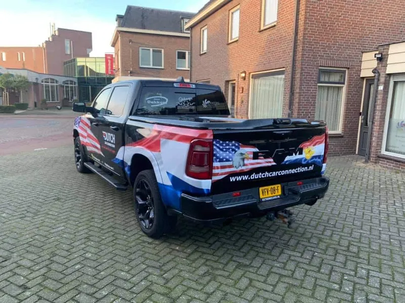 Zwarte pick-up van achteren met vlaggen-wrap en website op de laadklep