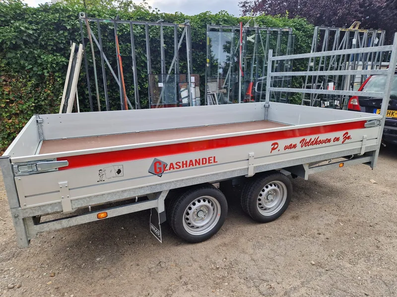 Open aanhangwagen met rode band, logo en belettering tussen glasbokken