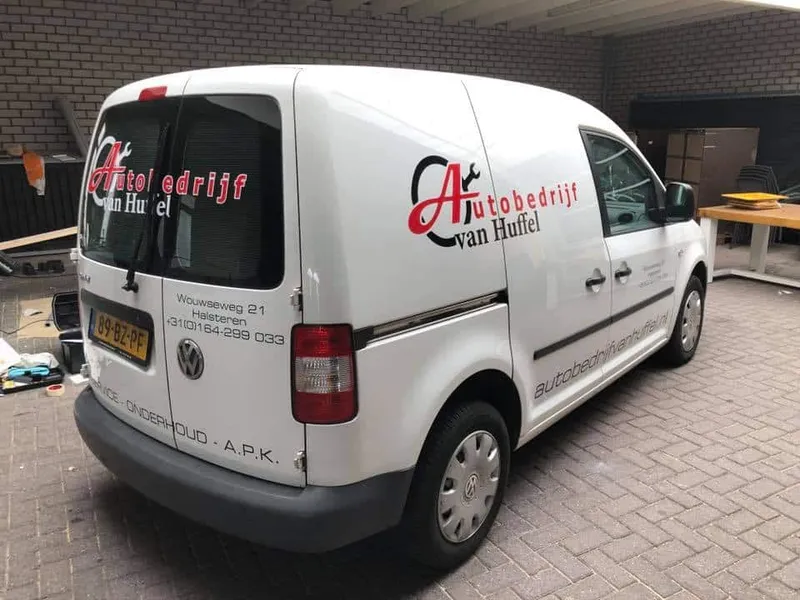 Witte bestelbus schuin van achteren met logo op zijkant en achterruit