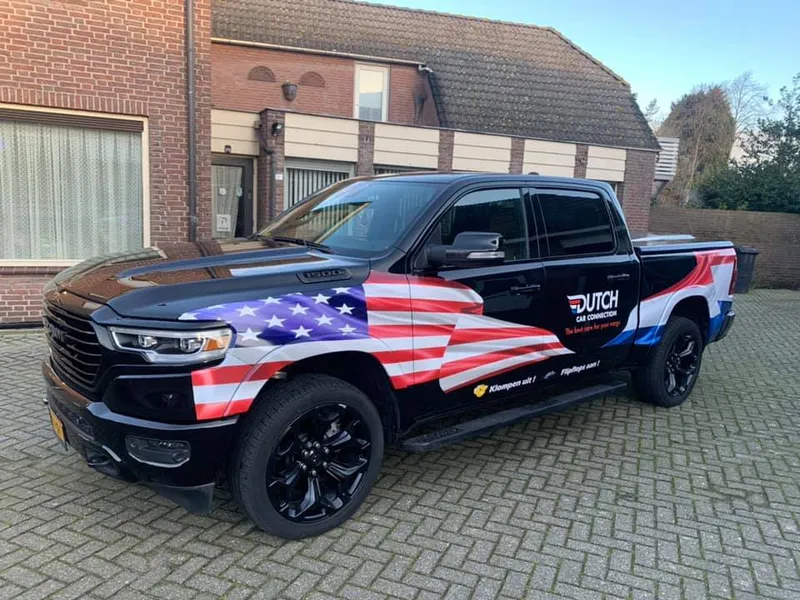 Zwarte pick-up schuin van voren met wrap van twee landenvlaggen op de zijkant