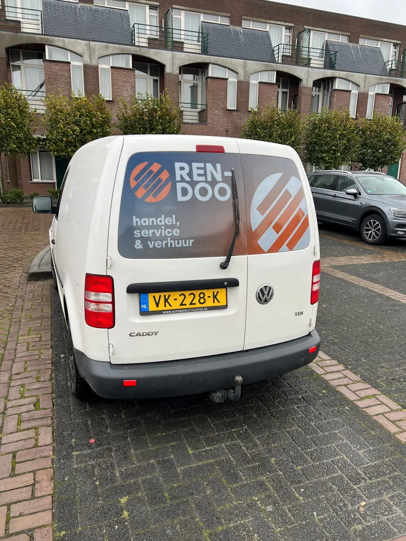 Witte bestelauto van achteren met bedrukte achterruit met logo en diensten