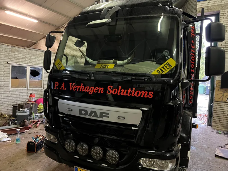 Zwarte vrachtwagen in een loods met rode belettering boven de grille en op de stijl