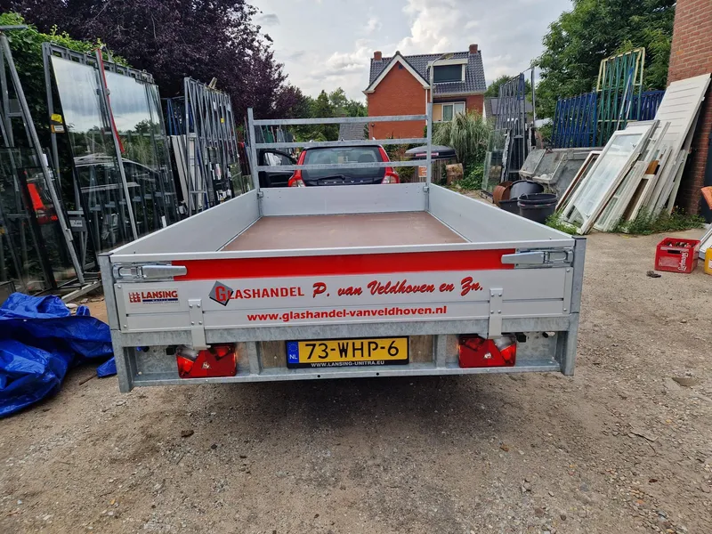 Open aanhangwagen van achteren met rode band, logo en website op de achterklep